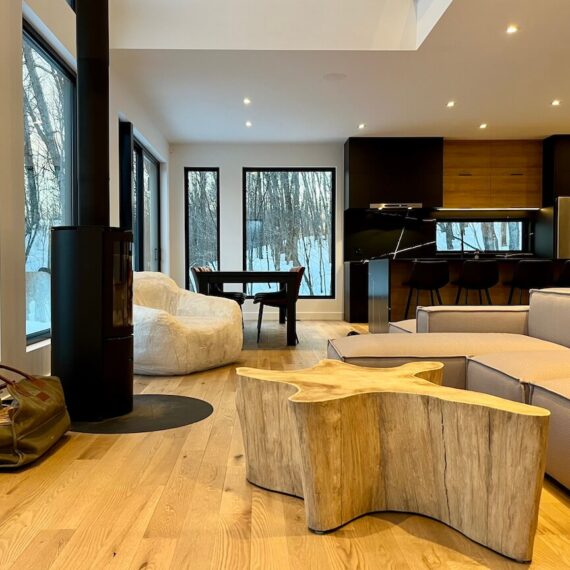 View of the open concept living room, kitchen and dining room with its wood stove, La Maison sur la falaise, Biophile architecture