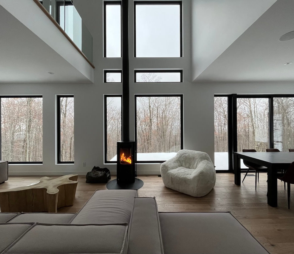 View of the open concept living space, living room and dining room with its wood stove, La Maison sur la falaise, Biophile architecture