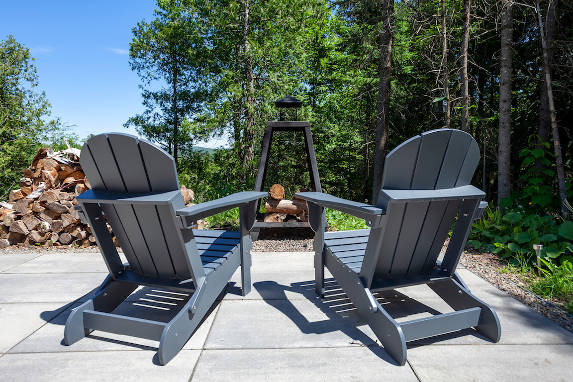 Vue de la terrasse côté sud-est avec chaises Adirondack et foyer au bois, projet La Grive réalisé par Biophile architecture